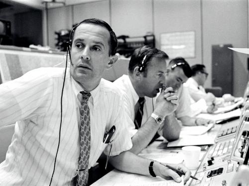 James A. Lovell, a white male NASA astronaut second from the foreground, monitors consoles during the descent of the Apollo 11 lunar module.