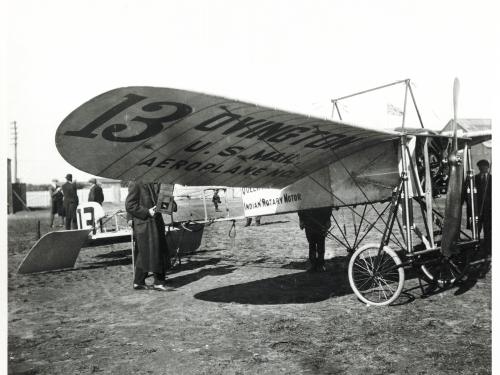 Side view of wooden and metal monoplane. Under the left wing, the plane is marked as owned by the "U.S. Mail".