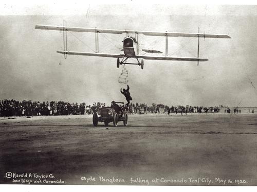 Front view of a biplane during an expedition flight. A person is trying to climb from an automobile below the biplane onto the biplane.