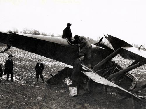 A crashed plane sits in a field and bystanders look at the plane.