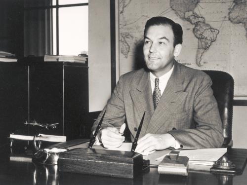 L. Welch Pogue, a white male chairman of the Civil Aeronautics Boards, poses informally as he sits at a desk.