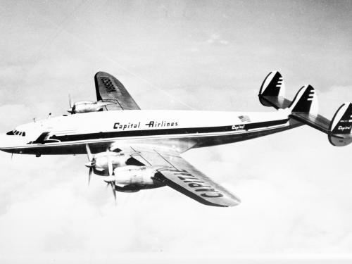 Side view of commercial aircraft in flight. Aircraft has four engines. Aircraft features "Capitol Airlines" name above the wings.