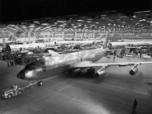 Side view of commercial jet inside a commercial jet factory. The plane is being towed by its front wheel.