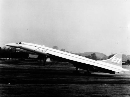 Artist's impression of the side view of a notably narrow aircraft with long back wings. The aircraft is taking off from an airport.