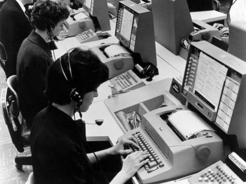 A group of people in an office setting use computers for airline reservations.