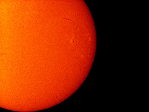 Partial disk view of the Sun featuring a sunspot on the right side of the Sun and a filament of plasma floating above the surface of the Sun.