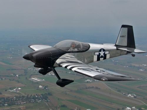 Side view of silver-colored, black, and white aircraft flying in the air with nonretractable landing gear.