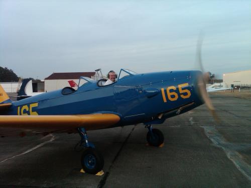 Side view of blue aircraft with one engine and yellow wings. Number "165" is painted in yellow on the nose and behind the cockpit.