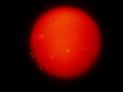 Disk view of the Sun's chromosphere with multiple sunspots and prominences of plasma rising from the chromosphere on the left side of the disk. Additional filaments of plasma floating above the chromosphere are visible on the bottom right quadrant of the disk.