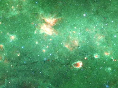 A partial view of a green-colored nebula inside the Milky Way with many orange-colored sections throughout.