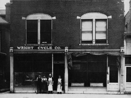 A brick, two-story bulding with a sign on a front facade labeling the building as "The Wright Cycle Co."