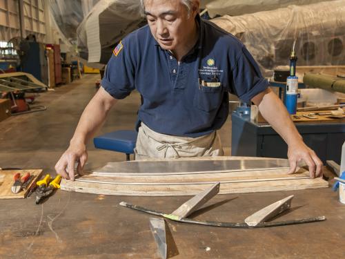 A male staff member of the museum's Collections Department works on restoring part of a World War II era bomber in the museum's restoration hangar.