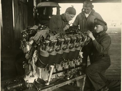 Three people examine a twelve-cylinder engine used for long-travel flight.