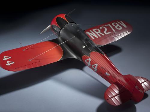 Top-facing view of a red and silver-colored monoplane model with one engine. The number 44 is painted on the left wing and behind the fuselage. Registration number NR278V is painted on top of the right wing.