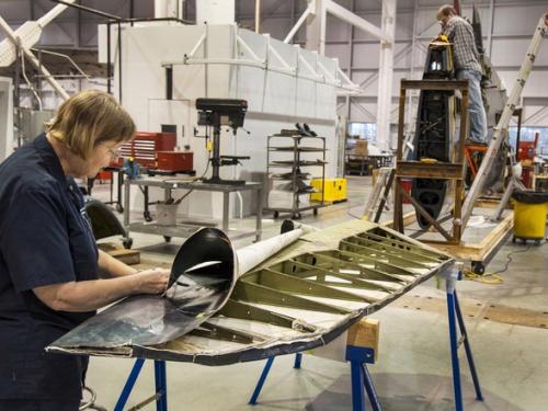 Two museum specialists perform conservation work on a blue military monoplane inside the Museum's restoration hangar.