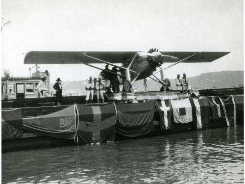 The Spirit of St. Louis sits on a barge as it is exhibited following Charles Lindbergh's record-breaking transcontinental flight. Flags are hung across the side of the barge.