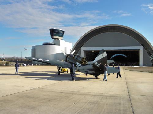 A group museum specialists work to move a gray and black monoplane into its permanent display spot inside the Museum's Steven F. Udvar-Hazy Center.