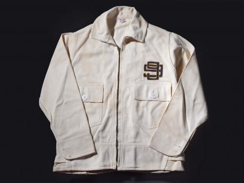 A white jacket intended for flight with a logo of two number nines interlocking on the left chest. The jacket features two pockets on the torso with one button each.