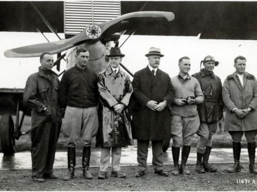 U.S. President Calvin Coolidge (a white man wearing a raincoat) stands with other white people at a meeting with pilots.