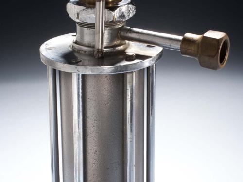 Metal rocket motor with cylinder base surrounded by metal support beams, which is attached to a bottom motor with tubes leading to two brass-colored nozzle halves and a third tube leading to a brass-colored horizontal ring.