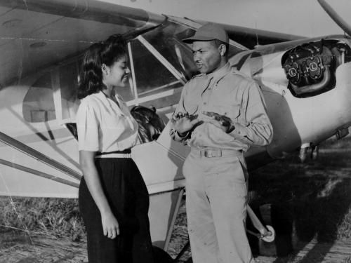 Two African American people stand in front of a small aircraft.