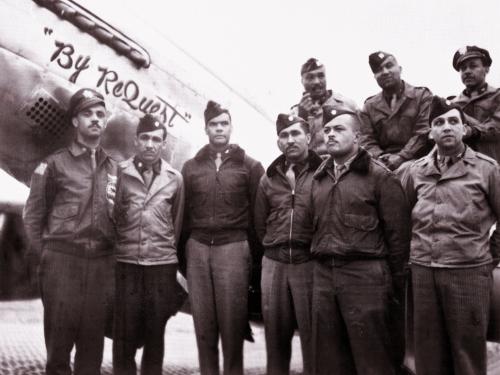 Benjamin O. Davis Jr., an African-American man standing third from the left, poses informally with members of his staff and other Tuskegee Airmen in front of a plane.