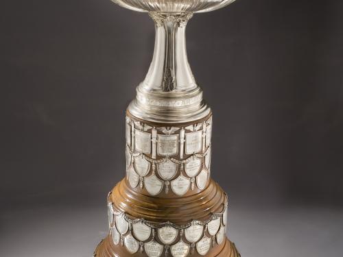 Aviation trophy with wooden tri-base holding military achievements on tiny plaques. The topper features four versions of Nike, Greek goddess of victory, holding a depiction of the Wright Military Flyer.