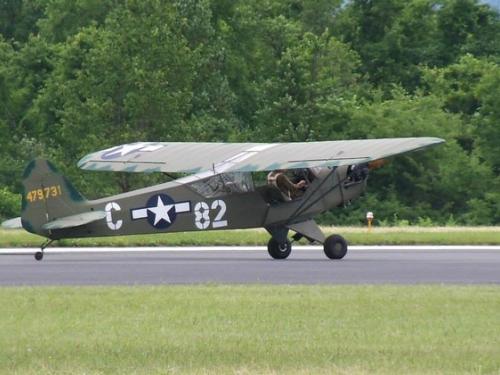 Side view of gray and green military monoplane with one engine.The letter "C" and number "82" are painted in white paint on the sides of a blue and white star emblem.