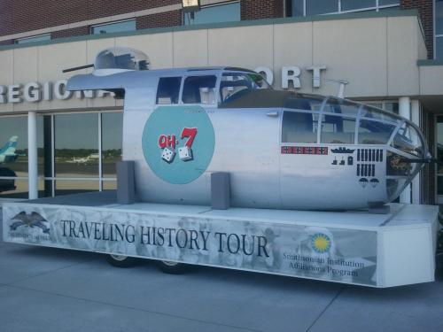 A plane's nose sits on a traveling exhibit trailer. The trailer has side detailing labelling it as part of a "traveling history tour".