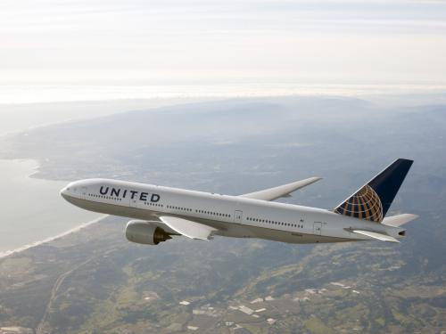 Side view of Boeing 777, a white commercial jet, in flight. The plane features white, blue, and yellow United Airlines livery.