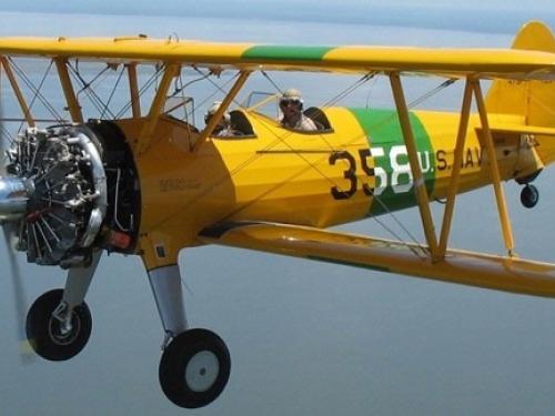 Side view of yellow and green biplane with single engine and fixed landing gear. Biplane is in flight.