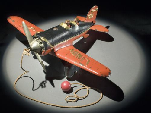 Top view of orange and black monoplane toy with a ball and string attached to the center of the propellors on the front.