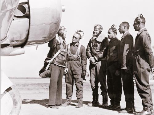 Five pilots who recently received their new status as Tuskegee pilots stand with another person next to a trainer aircraft.