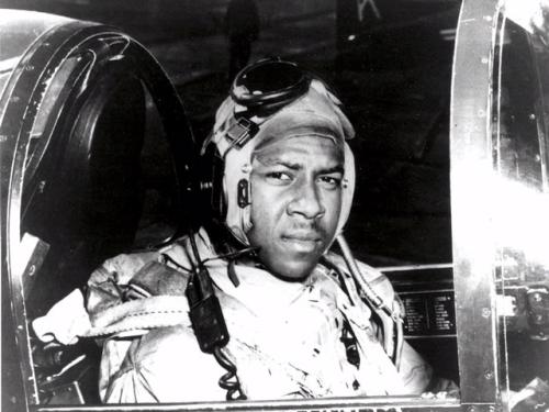 Jesse L. Brown, an African-American pilot who was part of the U.S. Navy, sits in the cockpit of an aircraft. He is wearing aviator gear.