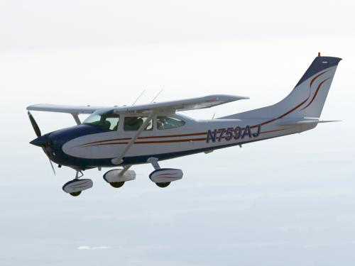 Side view of white monoplane in flight. Monoplane has one engine, fixed landing gear, and black and red accents. Registration number "N759AJ" is painted in black near the rear of the fuselage.