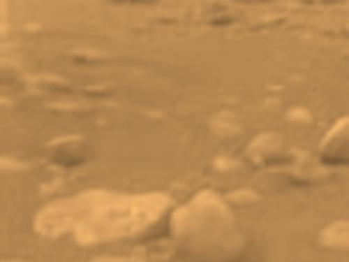 View of a part of the surface of Titan, a moon orbiting Saturn. The visible surface is rocky and is very uneven.