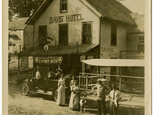 Harry Bingham Brown, a white male pilot, stands outside of a hotel named "Davis' Hotel" with other people.