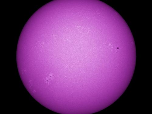 Purple disk view of the Sun's chromosphere featuring darker spots called sunspots and phages, or lighter clouds, across the visible section of the Sun.