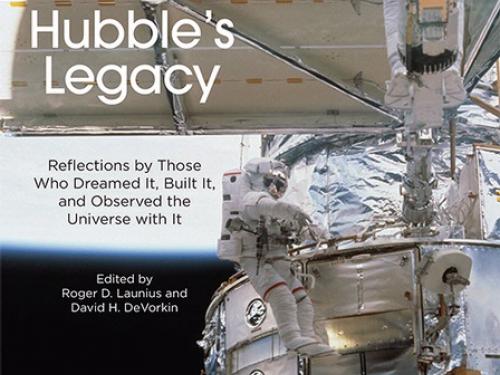 Book cover featuring a partial view of the Hubble Space Telescope in orbit as an astronaut performs a spacewalk next to the telescope. The book title "Hubble's Legacy" is placed on a solar panel that is perpendicular to the rest of the visible telescope.