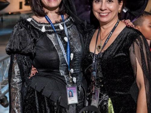 Two women wearing Halloween costumes pose behind a dish of candy at the Museum's annual Halloween event.