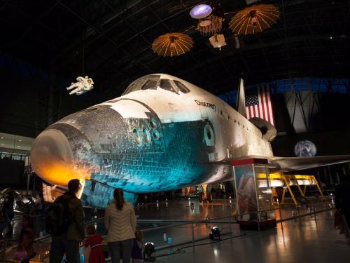 View of the Space Shuttle Discovery, a white space shuttle, with blue and orange lighting reflecting the Halloween mood at the Museum's annual Halloween event.