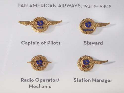 A set of four badges used by Pan American Airways during the 1930s and 1940s. Each badge features a dark blue circle surrounded by a golden circle. The golden circle usually features a small emblem highlighting each job position.