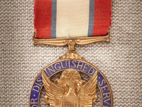 Purple and gold-colored metal medal with red, white, and blue-stripped ribbon. Front of medal features an eagle crest.