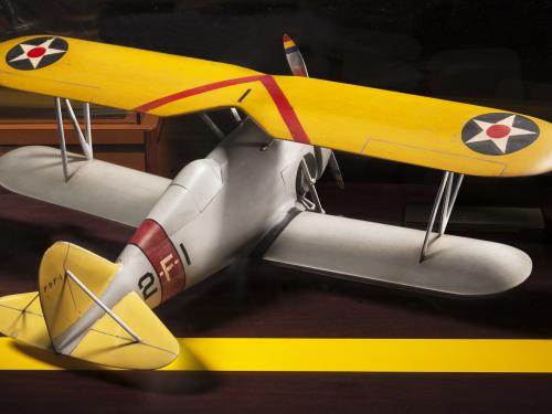 Back view of yellow and silver-colored biplane model aircraft. One white star inside a blue circle is featured on both sides of the top wing.