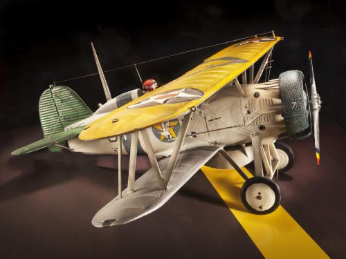 Side view of tan brown and yellow biplane model aircraft with one engine. 