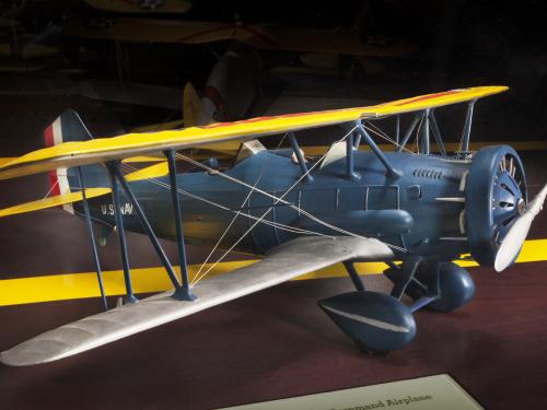 Side view of gray biplane model aircraft with yellow and silver-colored wings and one propellor.