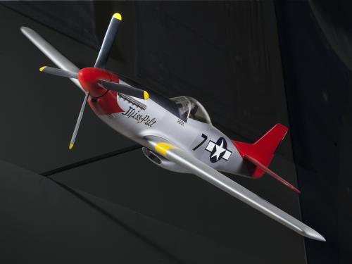 Frontal side view of silver-colored monoplane model aircraft with one engine and a red tail and nose. Blue and white star emblem is painted on the rear of the fuselage.