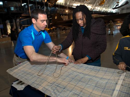 A Museum staff member assists two Museum visitors with activities at a table during an open house event.