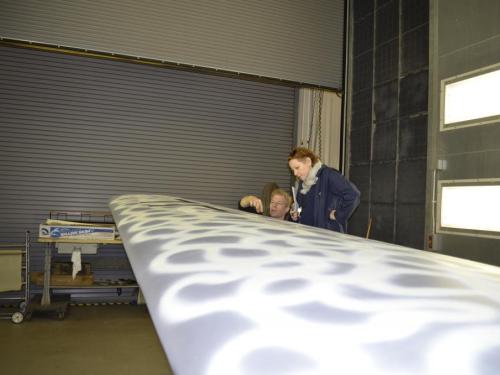 A Museum specialist and a Museum curator discuss the finished paint job on a silver-colored aircraft undergoing the restoration process.