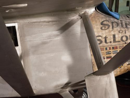 Close-up view of a side of the section below the cockpit of the Spirit of St. Louis, a silver-colored monoplane.